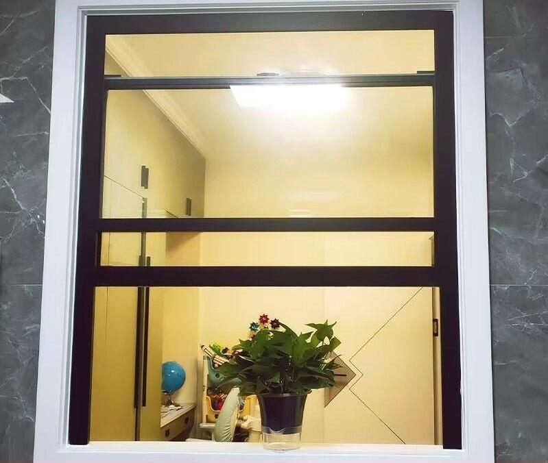 Moderne, enkelvoudig hangende, verticale schuiframen voor de keuken met zwart aluminium frame en roestvrijstalen ophangsysteem.